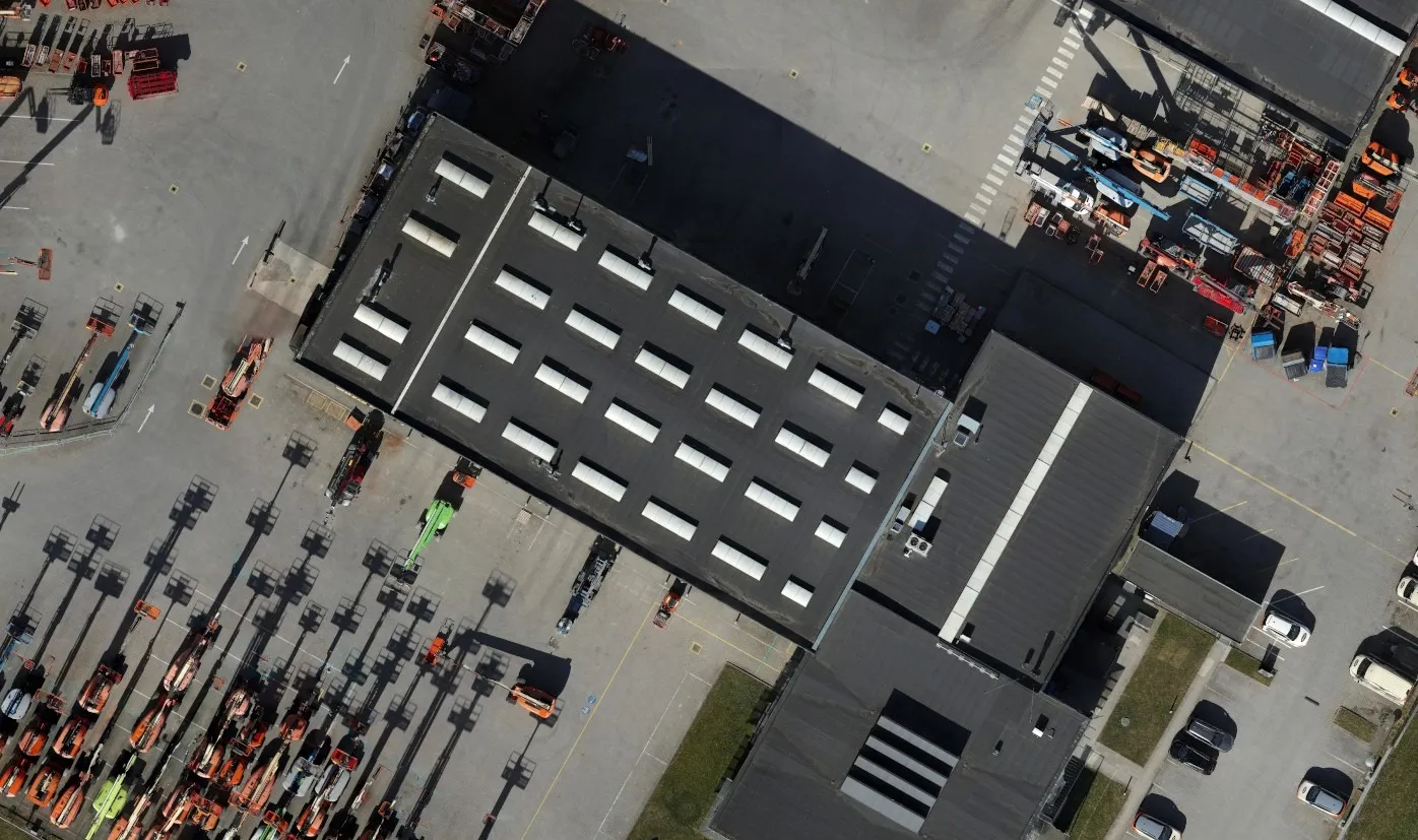 Nærbillede fra ortofotoet af tagfladerne på Riwals hovedbygninger med ovenlys og ventilationsenheder, omgivet af parkerede lifte